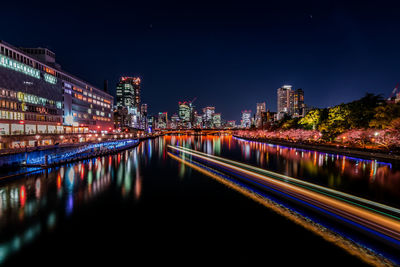 Illuminated city by river against sky at night