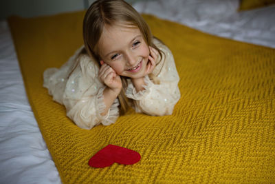 Cute smiling girl with heart shape lying on bed at home