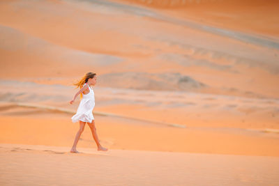 Woman standing on sand at desert against sky during sunset