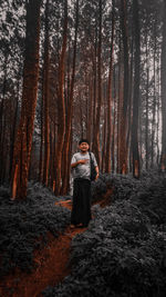 Full length portrait of young man standing amidst trees in forest