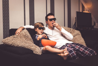 Father and son watching tv on sofa at home