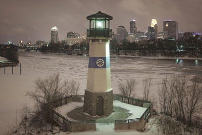 Illuminated tower by cityscape against sky at night