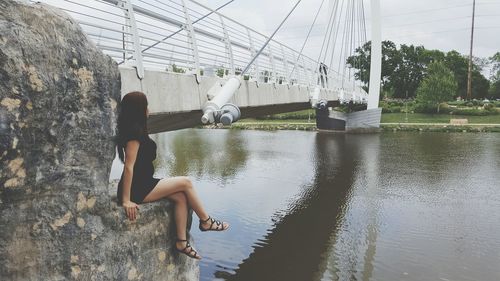 Woman sitting on rock formation by footbridge over river