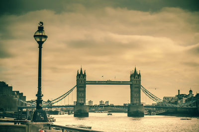 Tower bridge over river in city against cloudy sky