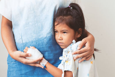 Girl embracing mother against wall in hospital