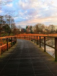 Footbridge amidst trees against sky during sunset