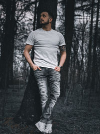 Young man looking away while standing on tree trunk