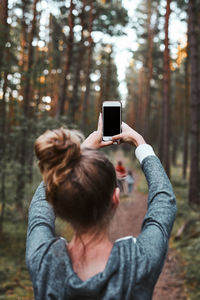 Rear view of woman photographing through smart phone in forest