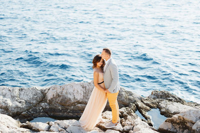 Side view of couple on rock by sea