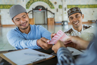 Smiling men receiving cash from person at mosque