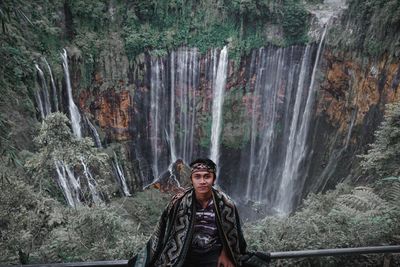 Portrait of man standing on rock against waterfall