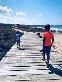 Rear view of friends walking on beach against sky