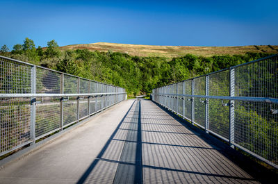 Footbridge over footpath amidst trees against sky