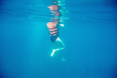 Low section of woman in swimwear swimming in blue sea
