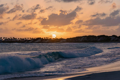 Waves rushing towards shore against sky during sunset