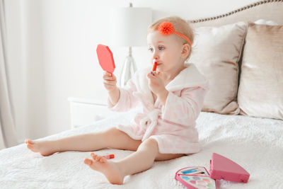 Cute girl applying make-up while sitting on bed at home