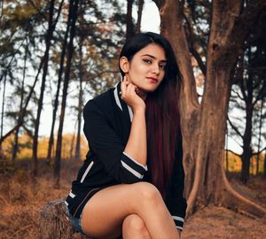 Portrait of beautiful woman with long hair sitting against tree in forest