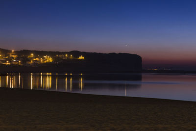 Illuminated city by sea against clear sky at night