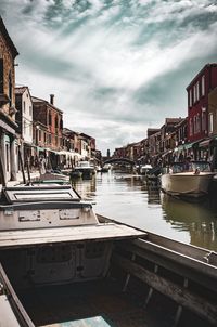 Sailboats moored on canal by buildings against sky in city