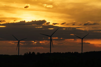 Silhouette windmills on land against sky during sunset