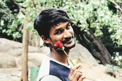 Portrait of young man with rose standing against trees