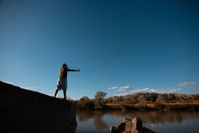 Man photographing by lake against sky