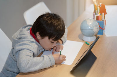 Rear view of boy sitting on table at home