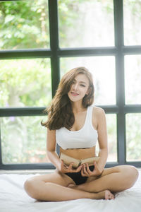 Portrait of young female model reading book on bed at home