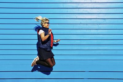 Full length of young woman jumping against blue wall