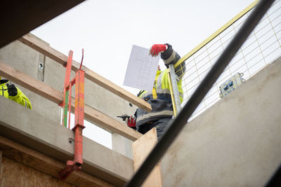 A construction worker is standing on a scaffolding with a walkie-talkie and a design drawing sheet