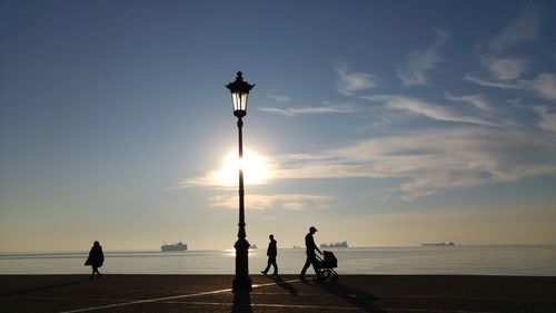 Silhouette people walking on footpath by sea at sunset