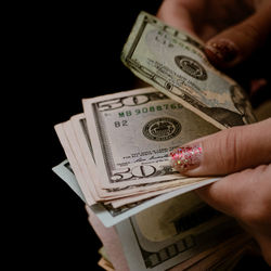 Cropped hand of person holding paper currency against black background