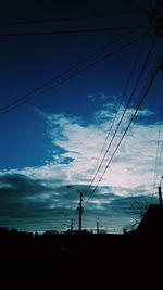 Silhouette of electricity pylon against cloudy sky