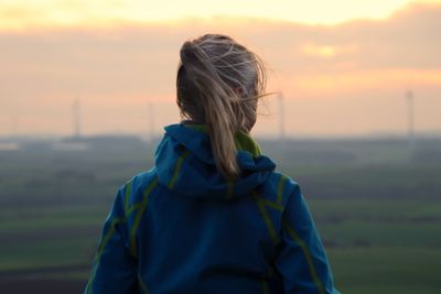 Rear view of woman standing on field against sky during sunset