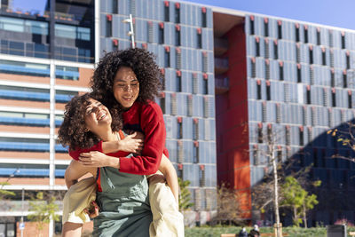 Lesbian woman carrying woman on back against building