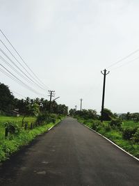 Road by electricity pylons against clear sky