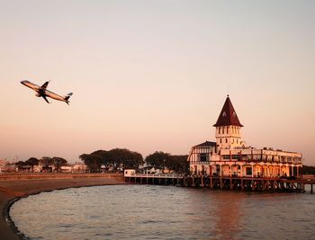 Airplane flying over river against sky during sunset