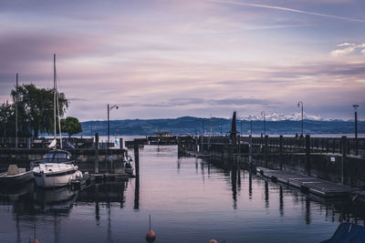 Sailboats moored in harbor at sunset