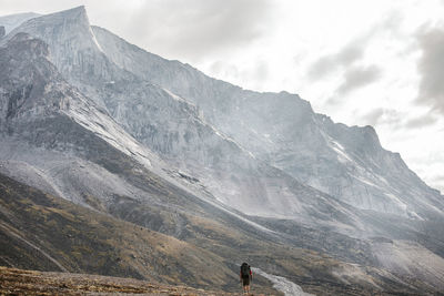 Backpacker is dwarf below massive granite mountain on baffin island.