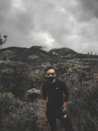 Portrait of man wearing sunglasses standing on mountain against sky