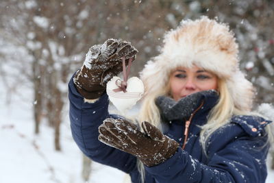 Woman wearing warm clothing while holding heart shape during winter