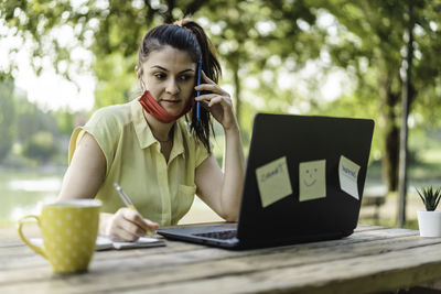 Mid adult woman using mobile phone while sitting on table