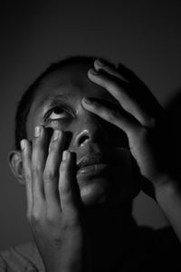 Young man with head in hands looking up against black background