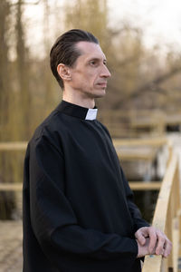 Serious mature priest standing by railing
