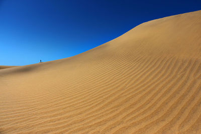 Sand dunes in desert against clear blue sky