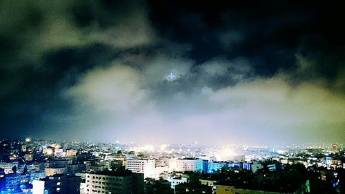 Illuminated cityscape against cloudy sky