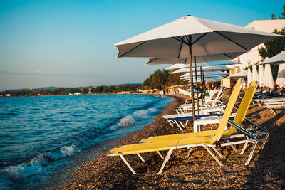 Lounge chairs and parasol at beach against sky