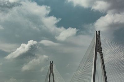 Low angle view of suspension bridge against cloudy sky