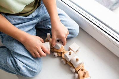 A preschooler boy plays with a wooden toy train on the windowsill