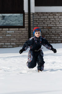 Boy running on snow covered yard during winter